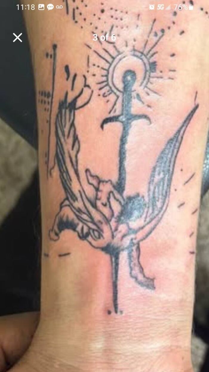 Abstract black ink tattoo on wrist featuring an anchor with wings and sunburst detail, unusual body art placement.