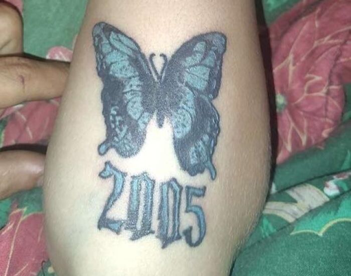 Butterfly tattoo with the year 2005 on a person's elbow, showcasing one of many unusual tattoos placed on skin.