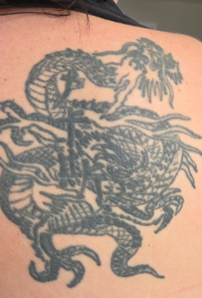 Black ink dragon tattoo covering a large portion of a person's upper back, a unique example of body tattoos.