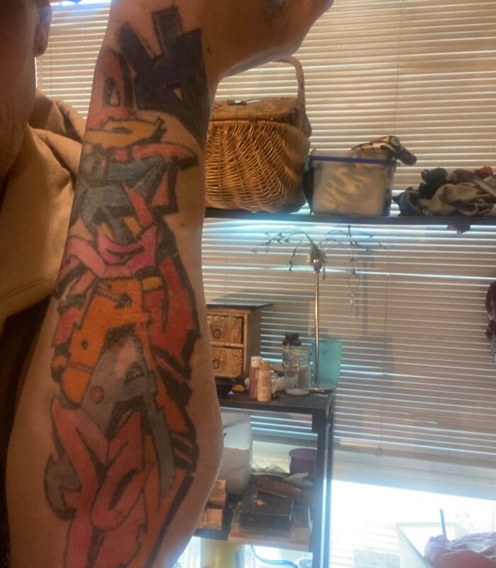 Colorful abstract tattoo covering forearm with assorted household items in background, example of tattoos people allowed on bodies.