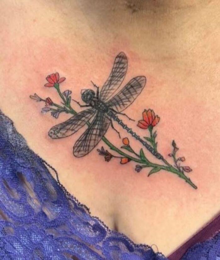 Close-up of a colorful dragonfly and flowers tattoo on a person's upper chest, showcasing unique tattoo designs.