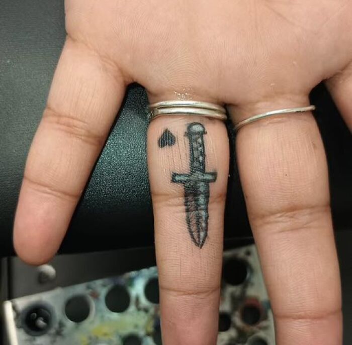 Finger tattoo of a dagger and a small spade symbol, showcasing an unusual design people allowed permanently on their bodies.