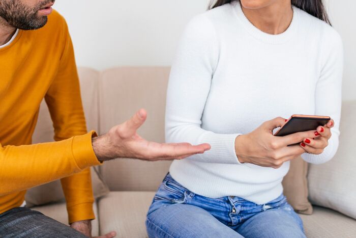 Couple sitting on sofa with woman holding phone and man gesturing, illustrating toxic relationship traits and conflict.