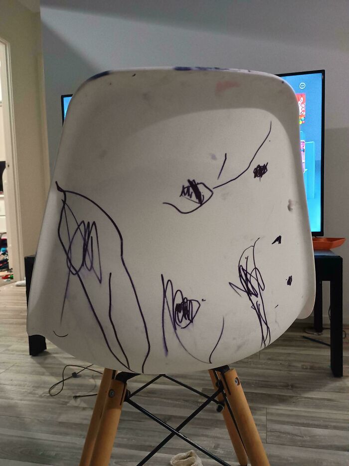 White chair with black marker scribbles by family members, showing frustration in a home setting.