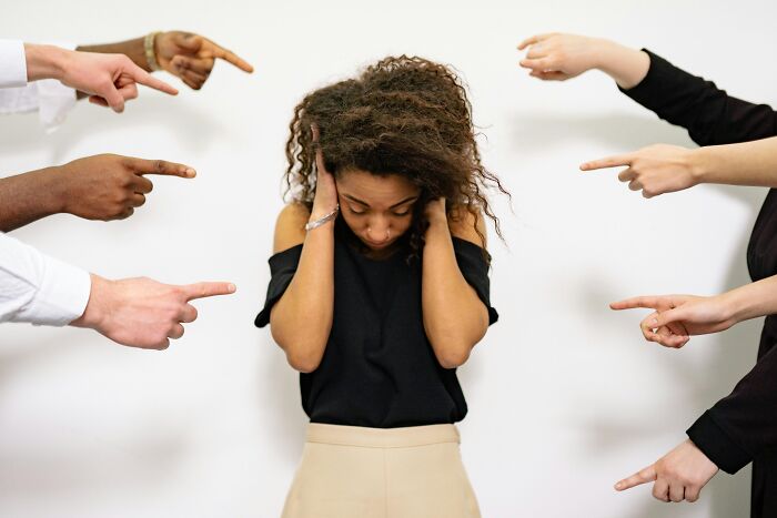 Young woman covering ears while multiple hands point at her, illustrating toxic relationship traits causing stress and anxiety.