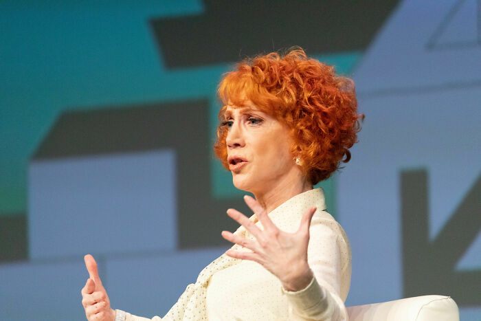 Kathy Griffin with red hair speaking passionately during a live event, highlighting her bio and career achievements.