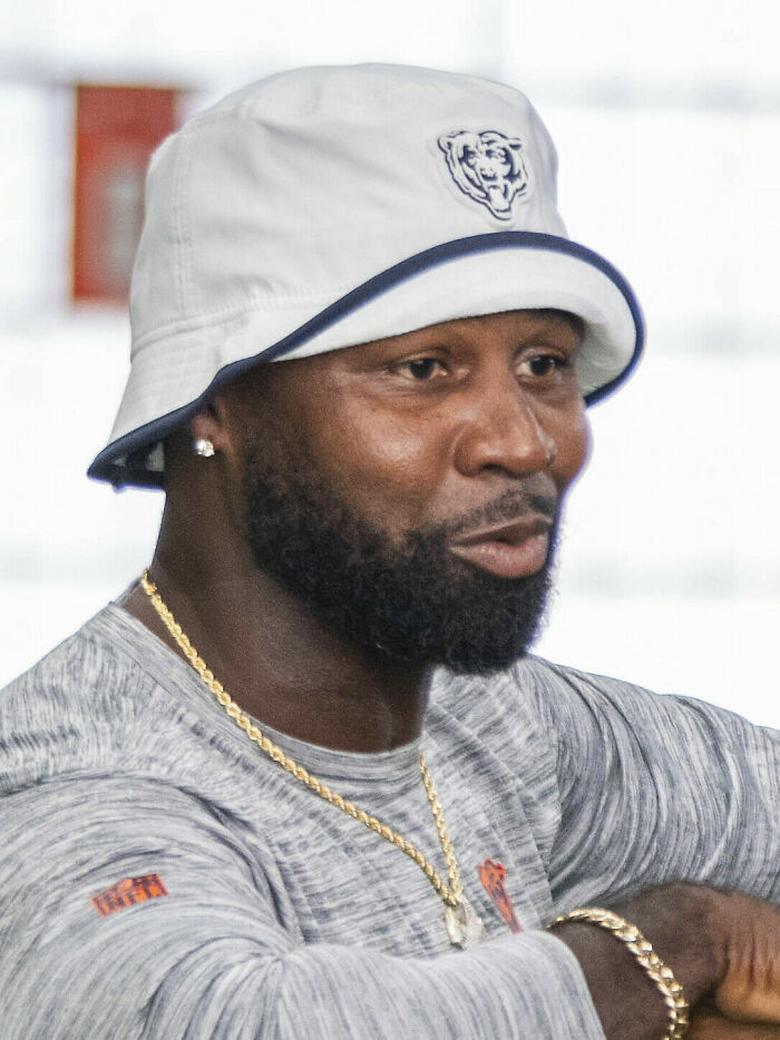 Devin Hester wearing a white bucket hat and gray shirt, engaged in a casual conversation indoors.