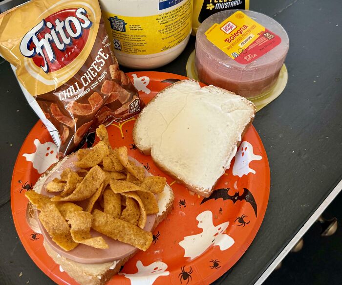 Girl dinner combo with bologna sandwich and chili cheese Fritos on a Halloween-themed plate.