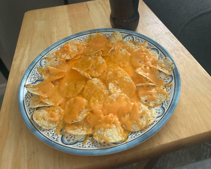 Plate of chips topped with melted cheese, a simple and popular girl dinner combo on a wooden table.