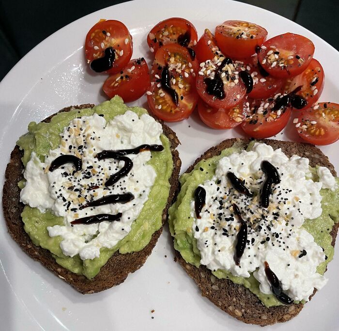 Avocado toast with cottage cheese and balsamic glaze paired with cherry tomatoes sprinkled with seasoning, a classic girl dinner combo.