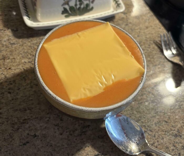 Bowl of tomato soup with a slice of processed cheese on top, representing iconic girl dinner combos.