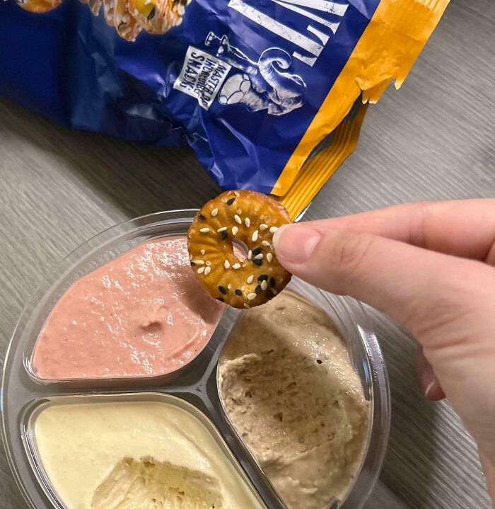 Hand dipping sesame cracker into hummus and dip combo, showcasing iconic girl dinner snack ideas and combos.