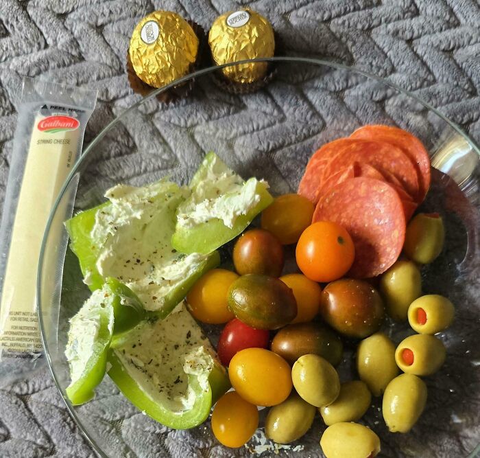 Plate with green pepper stuffed with cream cheese, assorted cherry tomatoes, olives, pepperoni, string cheese, and chocolates, girl dinner combos.