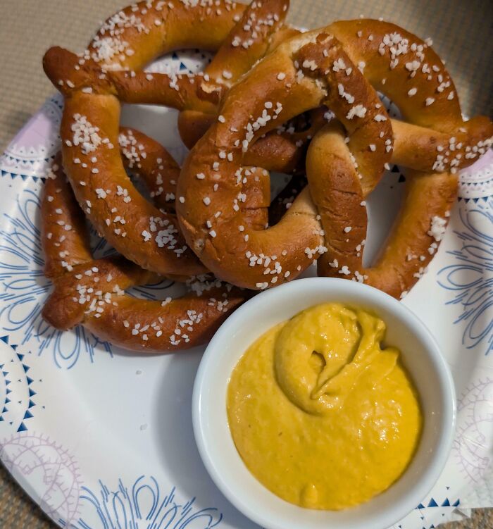 Soft pretzels sprinkled with salt served with a mustard dip as a popular girl dinner combo on a patterned plate