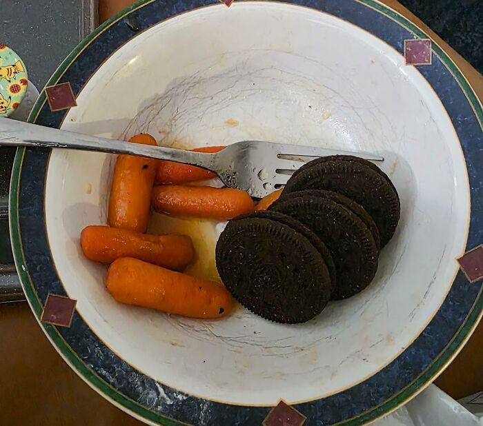Bowl with baby carrots and Oreo cookies fork showing an iconic girl dinner combo with unusual food pairings.