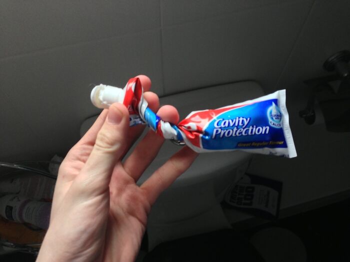 Hand holding a twisted tube of toothpaste, illustrating people with zero common sense surviving everyday tasks.