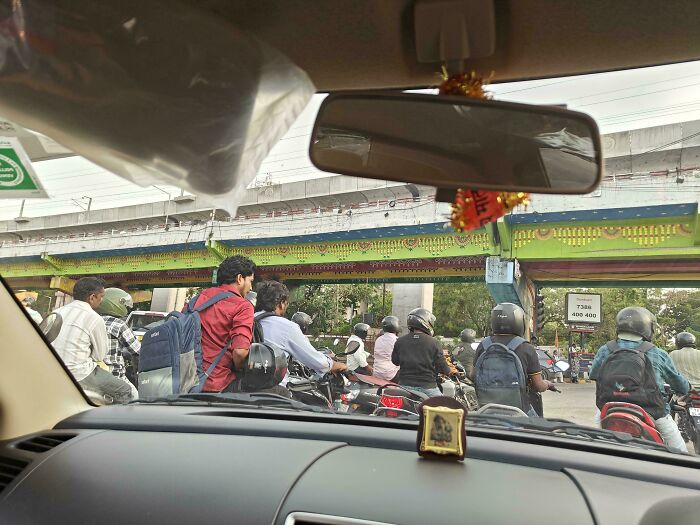 View from inside a car showing people with zero common sense riding motorcycles without helmets on a busy road.