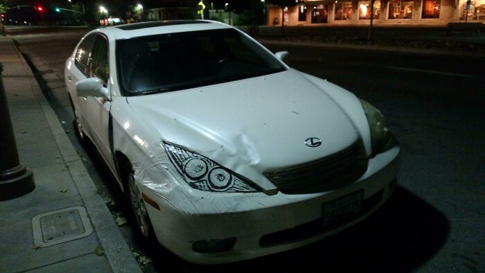 White sedan with front damage parked on a city street at night, showcasing lack of common sense in driving mistakes.
