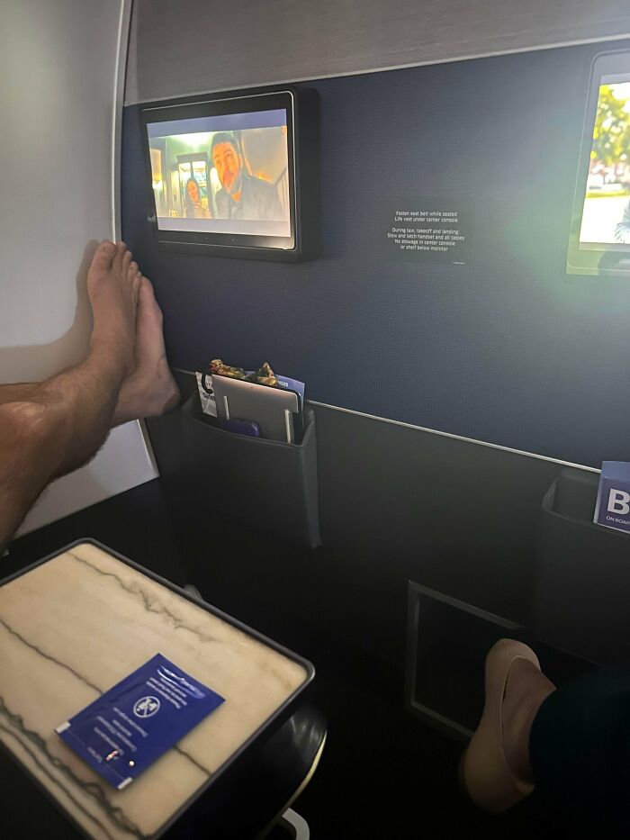 Feet on airplane seat screen showing lack of common sense by people making others wonder how they survived this long.