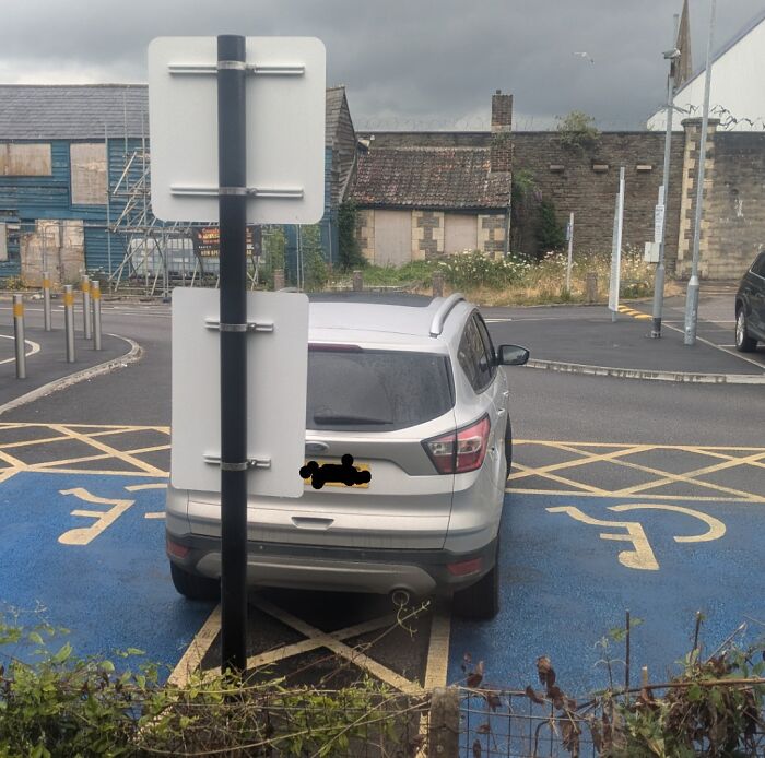 Silver SUV parked incorrectly across multiple disabled spots behind a confusing signpost showing zero common sense parking fail.