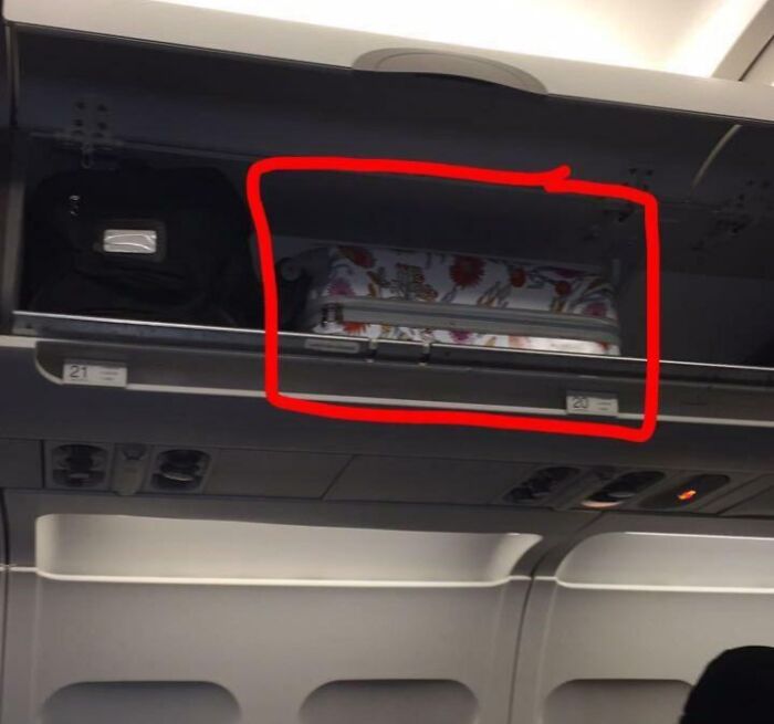 Suitcase placed sideways blocking airplane overhead luggage space, showing lack of common sense and poor packing skills.