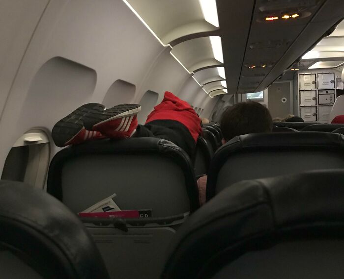 Passenger lying on airplane seats with feet up, showing lack of common sense during flight.