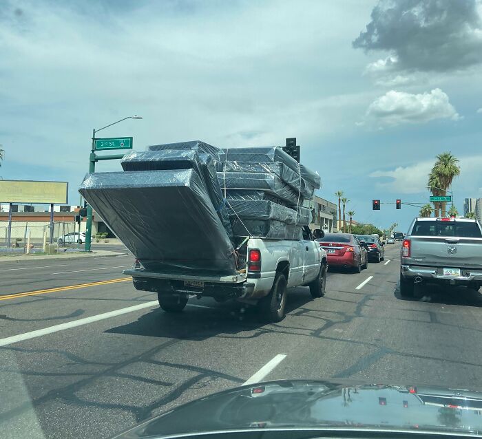 Pickup truck dangerously overloaded with mattresses on city street, showing lack of common sense and risky behavior.