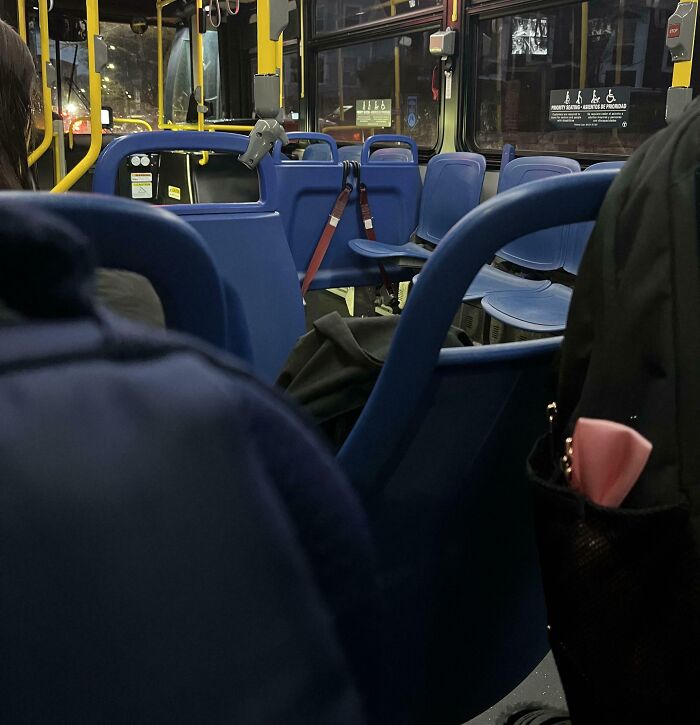 Interior of a public bus with blue seats and a backpack placed in an unusual way, showing zero common sense behavior.