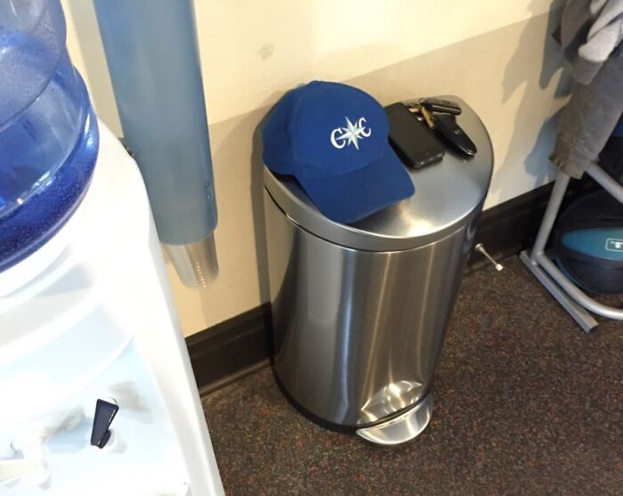 Blue cap, phone, and keys placed on a closed trash can next to a water cooler, showing lack of common sense.