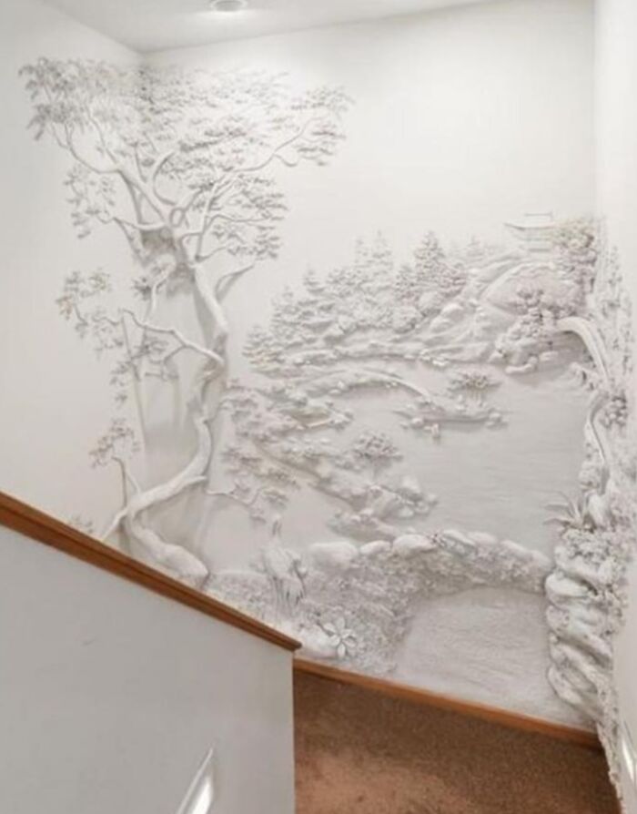 Intricate white 3D wall art in a home, showcasing detailed nature scene with trees and landscape on stairway wall.