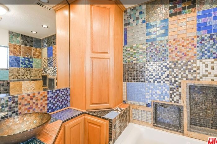 Bathroom with colorful mosaic tiles, wooden cabinets, and a unique sink in a Zillow home to see.