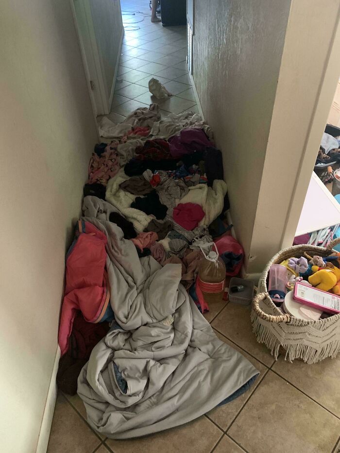 Pile of clothes and blankets blocking a narrow hallway, showcasing a family-related mess causing frustration to vent online.