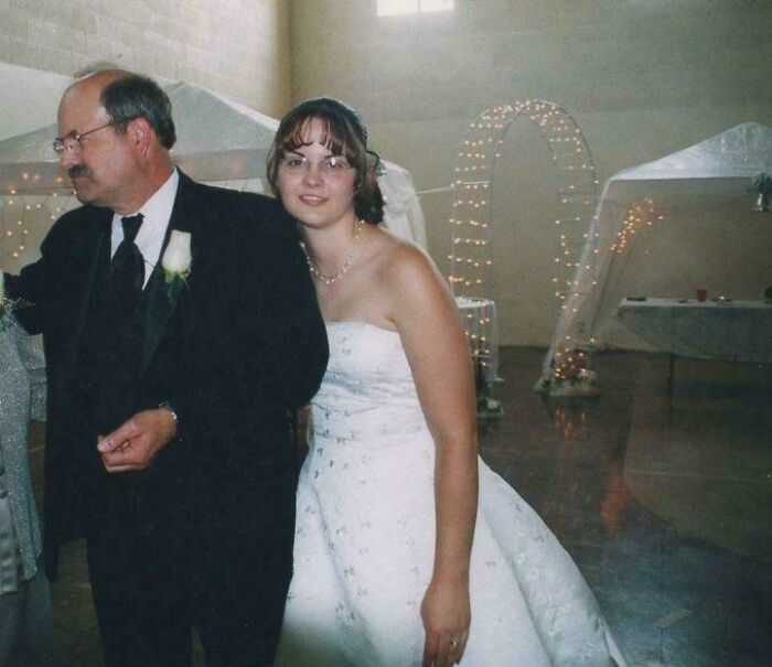 Bride in white wedding dress with an older man in a suit at a decorated venue in a unique historical photo.