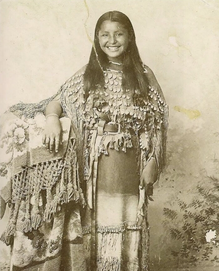 Young Native American woman in traditional attire posing for unique historical photo with a deep backstory, vintage sepia tone.