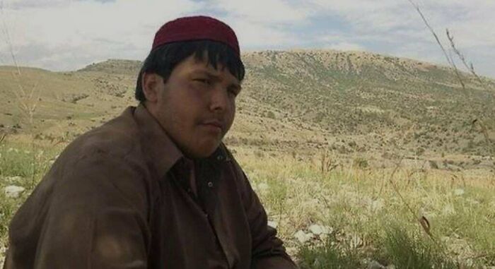 Young man wearing traditional clothing sitting outdoors in a remote landscape captured in unique historical photos.