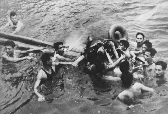 Group of men in water rescuing a person using a flotation device in an utterly unique historical photo with deep backstory.