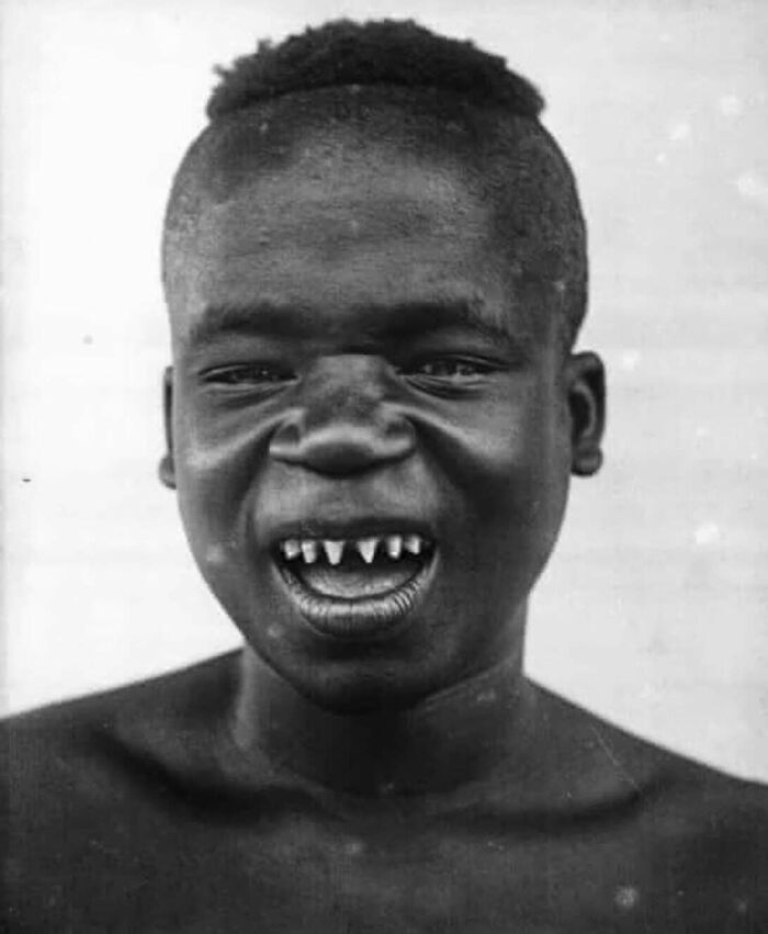 Unique historical photo of a man with sharpened teeth smiling in a black and white vintage portrait.