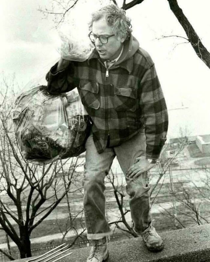 Man wearing glasses and plaid jacket holding a garbage bag in an utterly unique historical photo with a deep backstory