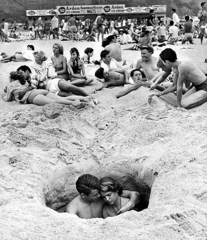 Couple buried together in a deep hole on a crowded beach, a unique historical photo with a deep backstory.