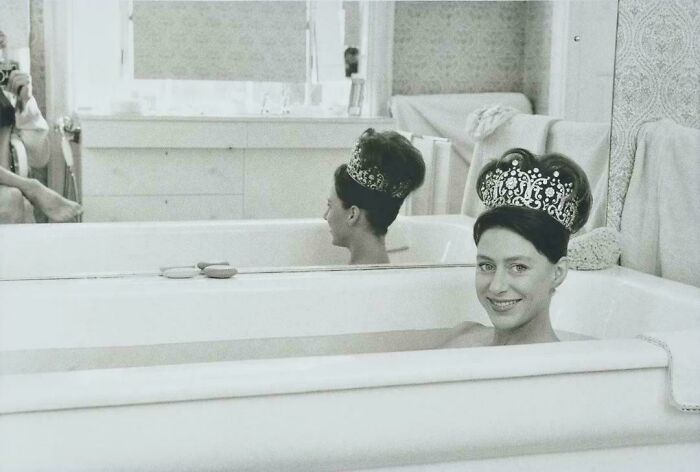 Young woman wearing a large jeweled crown, smiling while sitting in a bathtub, unique historical photo with a deep backstory.