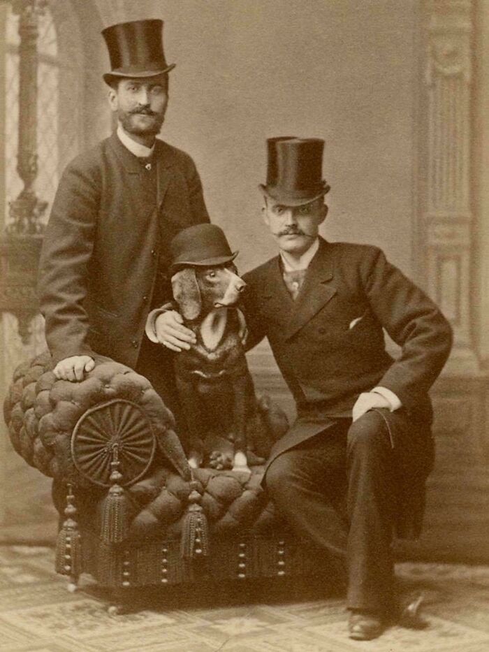 Two men and a dog wearing hats seated on a vintage couch in a unique historical photo with a deep backstory.