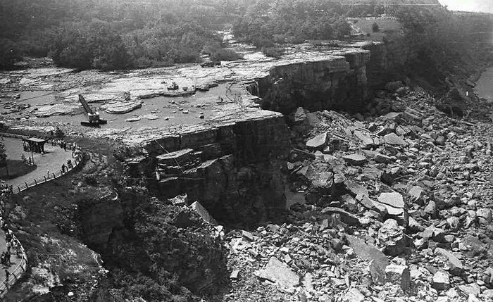 Black and white historical photo showing a collapsed cliffside with rubble and onlookers near the edge of the wreckage.