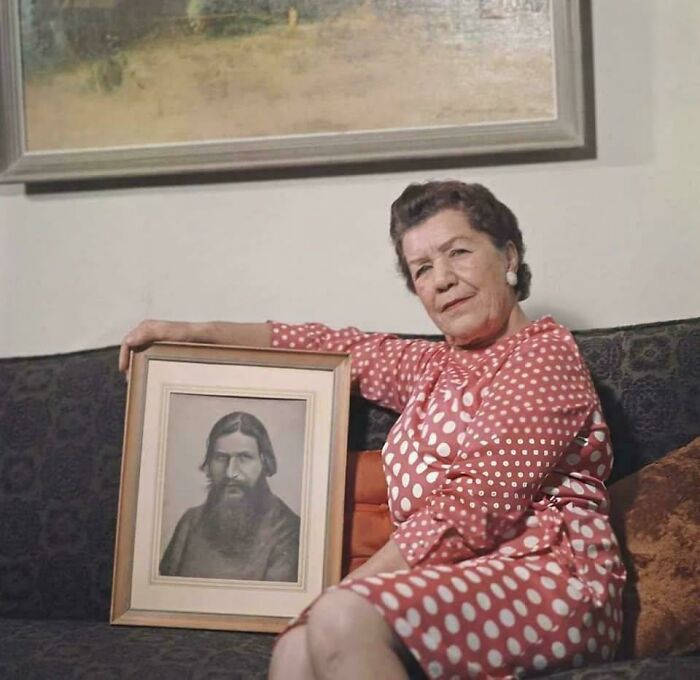 Woman in a polka dot dress sitting on a couch holding a framed historical photo with a deep backstory.