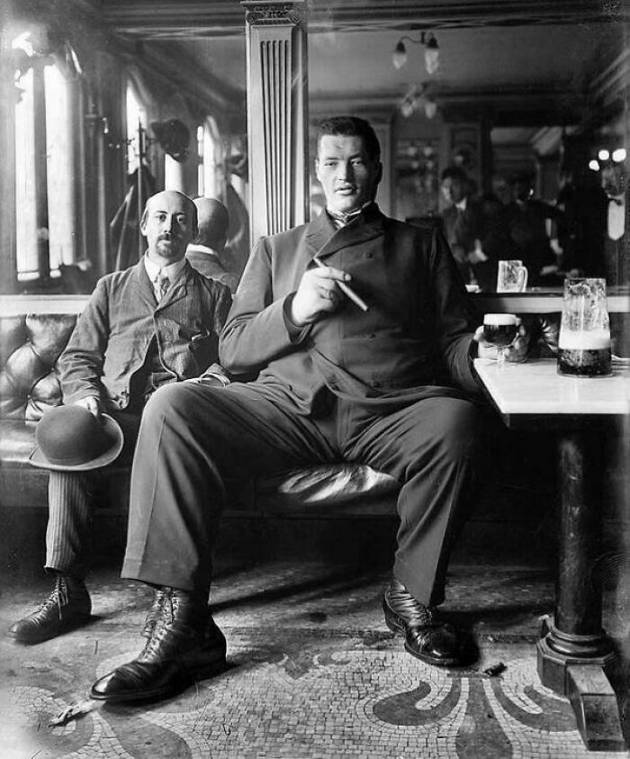 Black and white historical photo of a giant man seated with a cigar and a drink, showcasing unique historical photos with deep backstory.