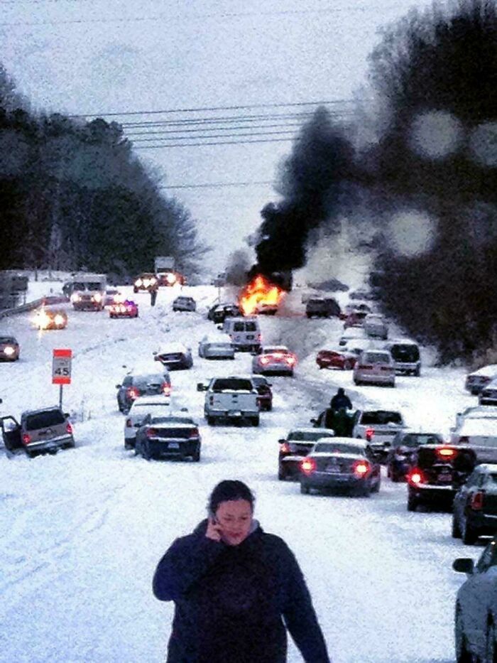 Person walking on snowy road with multiple vehicles and a burning car in traffic, unique historical photos scene.