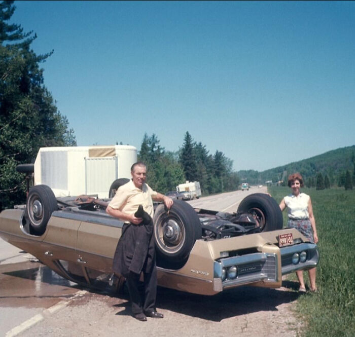 Man and woman stand beside an overturned car on a rural road in a unique historical photo with a deep backstory.