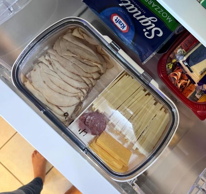 Clear kitchen storage container with deli meats and cheese neatly organized inside a refrigerator drawer.