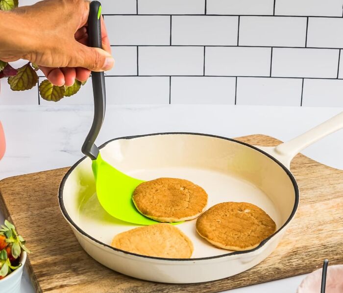 Hand holding a green spatula flipping cookies in a white pan, showcasing new kitchen finds and cooking tools.