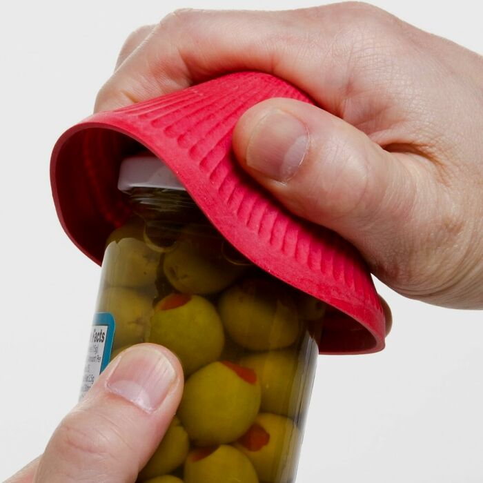 Hand using a red silicone gripper to open a jar of green olives, a new kitchen find trending for ease of use.