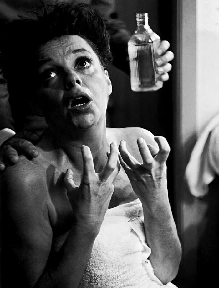 Black and white historical photo of distressed woman with raised hands and bottle held by another person behind her.